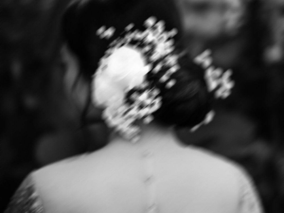 Pengantin wanita menghadap ke belakang, menunjukkan detail indah dari gaun pernikahannya dengan latar pemandangan matahari terbenam.